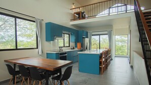 A modern kitchen with a dining area, a staircase, and a view of trees. - Brand new 4BR, 3BA ocean-view villa with shared pool in Nosara (Nosara)