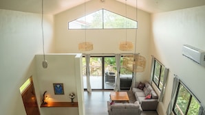 A spacious living area with a high ceiling, a dining table, a sofa, and a staircase. - Brand new 4BR, 3BA ocean-view villa with shared pool in Nosara (Nosara)