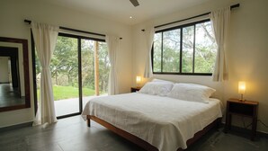 A spacious bedroom with a large bed, two bedside tables with lamps, a ceiling fan, and a sliding glass door leading to a balcony. - Brand new 4BR, 3BA ocean-view villa with shared pool in Nosara (Nosara)
