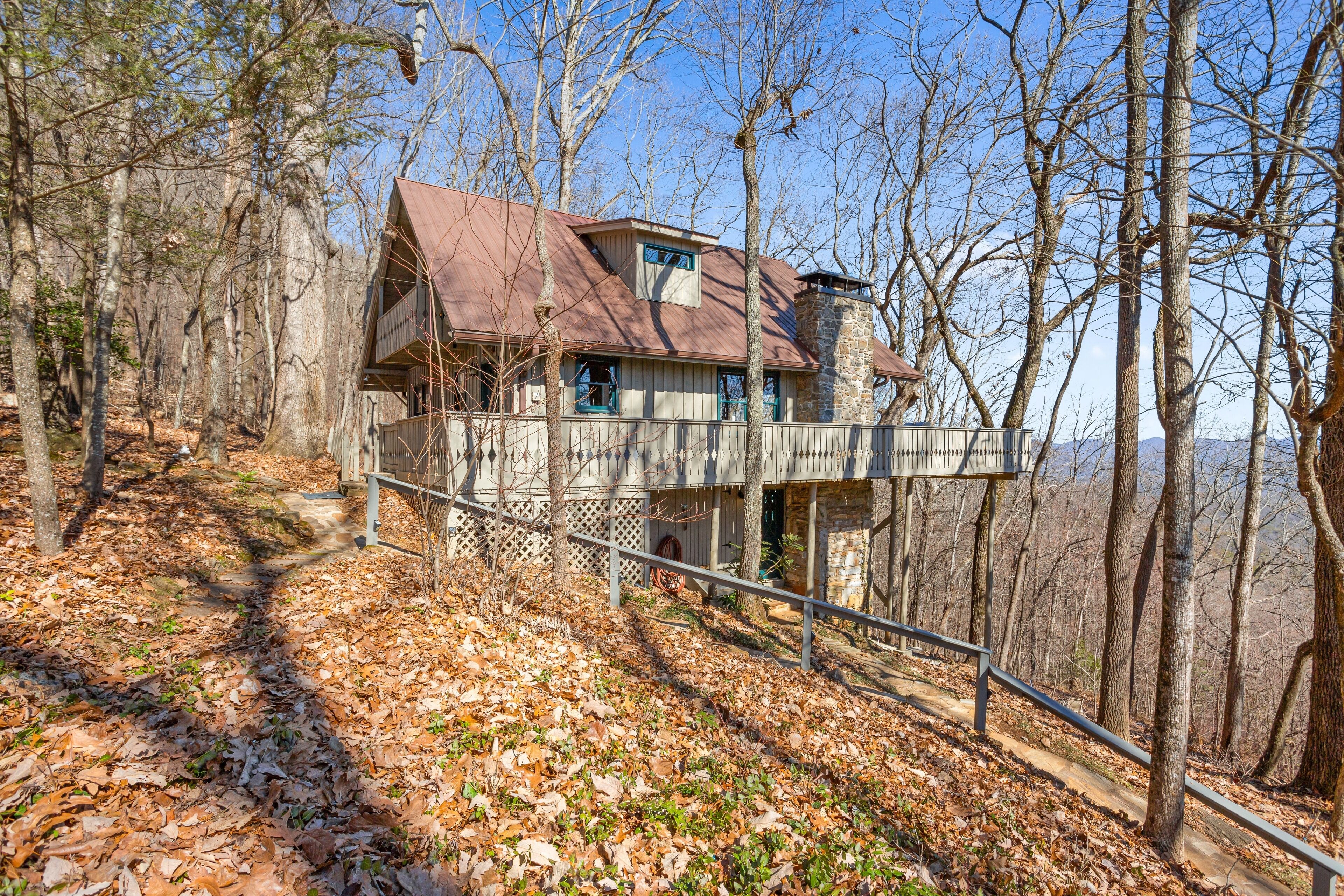 A cabin with a stone foundation, a metal roof, and a balcony overlooking a forested area.