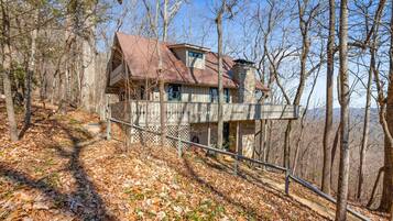 A cabin with a stone foundation, a metal roof, and a balcony overlooking a forested area.