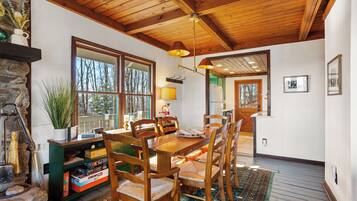 A wooden dining table with chairs, a stone fireplace, and a large window with a view of trees.