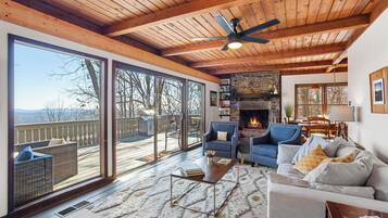 A spacious living room with a fireplace, large windows, and a deck.