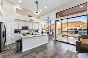A modern kitchen with white cabinetry, a central island, and a dining area with a view of a mountain and water.
