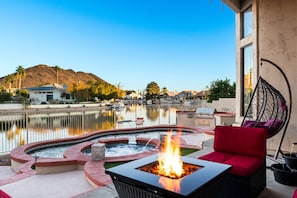 Eine Terrasse mit Feuerstelle, Sitzgelegenheiten und Blick auf einen See und ein Gebirge.