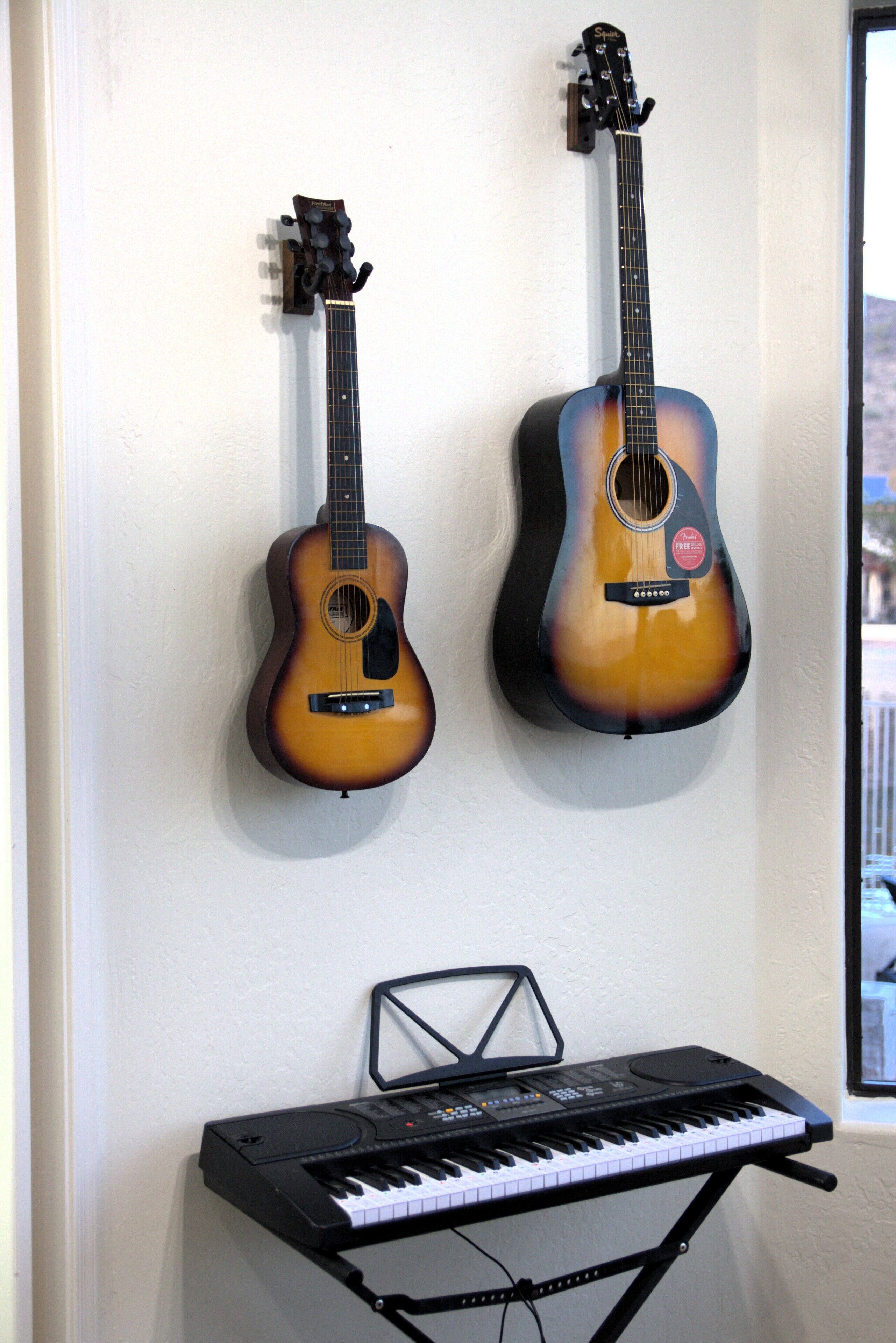 Dos guitarras colgadas en una pared y un teclado sobre un atril debajo.