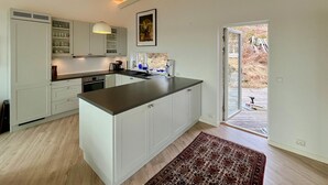 Cocina moderna con armarios blancos, una isla central y vistas a una terraza exterior.
