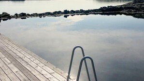 Un muelle de madera se extiende sobre aguas tranquilas, con una escalera metálica que da al agua.