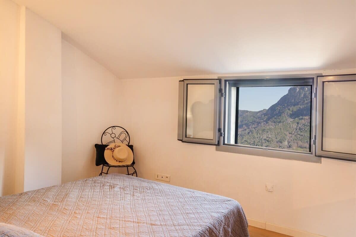 A bedroom with a bed, a chair, and a window with a mountain view.