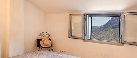 A bedroom with a bed, a chair, and a window with a mountain view.