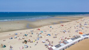 Une plage avec de nombreuses chaises longues et des parasols, un bateau et un ciel dégagé.