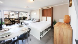 Une chambre moderne avec un lit, une table de chevet et une vue sur la ville grâce à de grandes fenêtres.