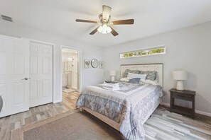 A bedroom with a bed, bedside tables, a ceiling fan, and a view of a bathroom. - A 3-bedroom lake-side cottage at Sunnyside with a fenced yard, sleeps up to 6. (Greenbush)