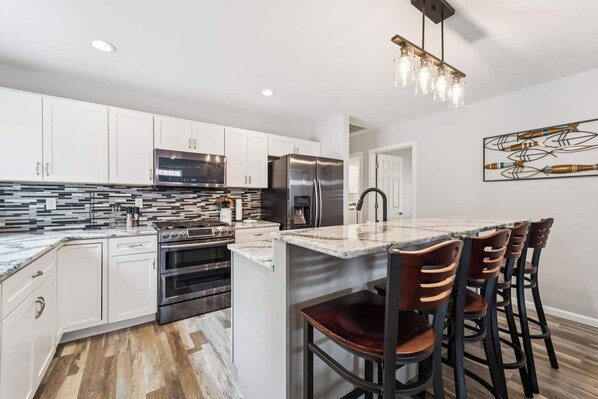 A modern kitchen with white cabinets, stainless steel appliances, and a marble countertop.