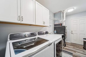 Ein Waschbereich mit einer Samsung Waschmaschine und einem Trockner, weißen Schränken und Holzboden.