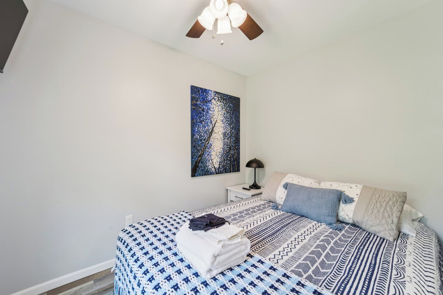 A bedroom with a bed, a nightstand, a lamp, and a painting on the wall.