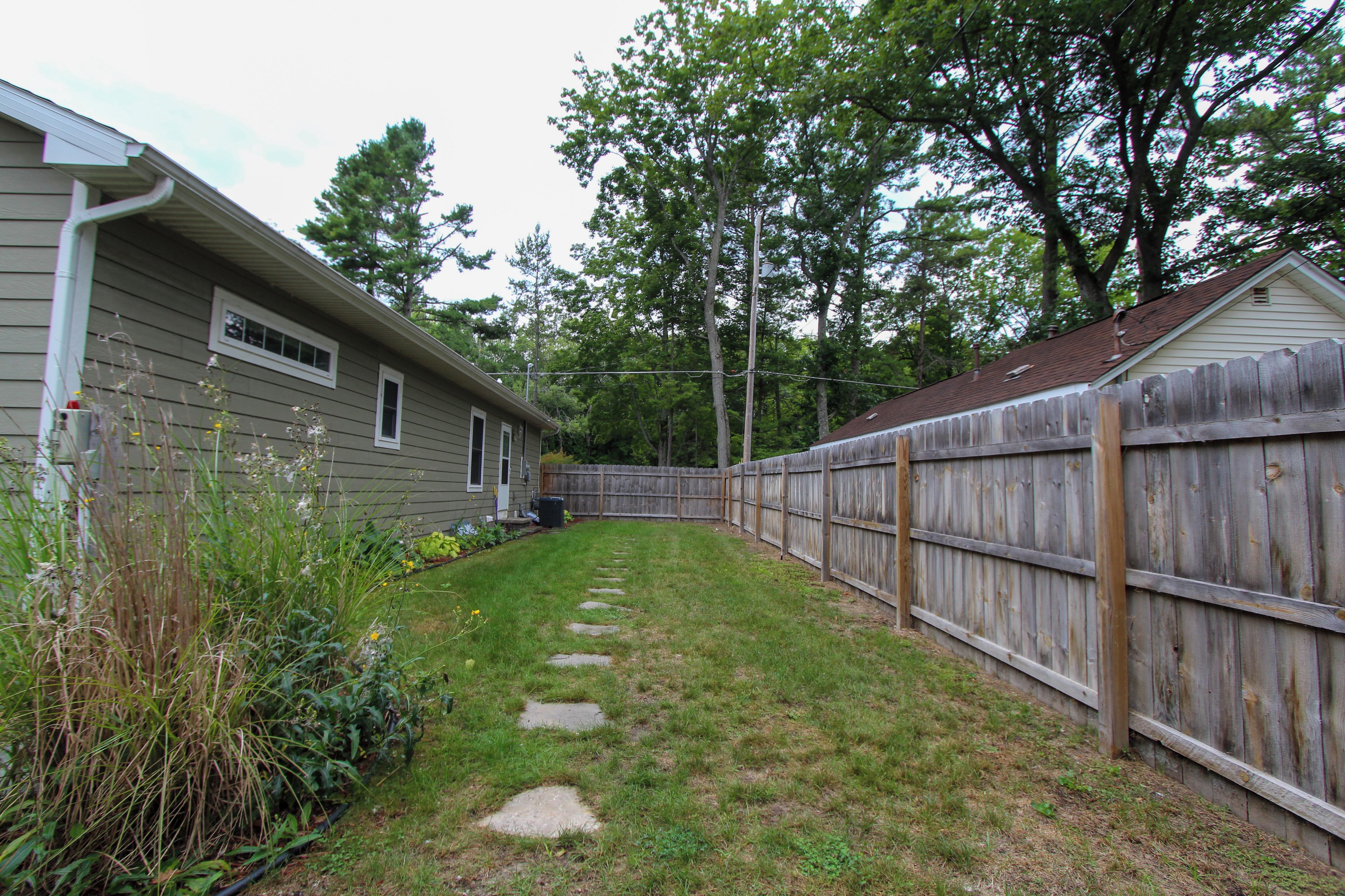 A residential backyard with a wooden fence, a grassy lawn, and a house with siding.