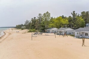 Uma praia com areia, uma rede de voleibol e várias cadeiras de praia.