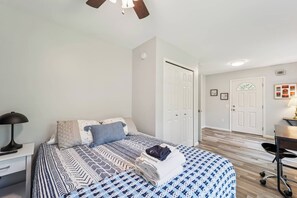 Ein Schlafzimmer mit Bett, Nachttisch, Lampe und einer Tür zu einem anderen Raum.