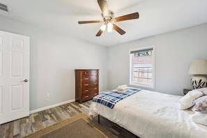 Un dormitorio con cama, cómoda, ventilador de techo, ventana y lámpara.