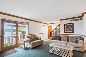 A living room with a sofa, armchair, coffee table, and a staircase leading to another room. - Book multiple lakefront cottages at Sunnyside, from cozy studios to a 4BR home. (Greenbush)