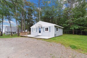 A single-story cabin with a front porch, surrounded by trees and a gravel driveway. - Book multiple lakefront cottages at Sunnyside, from cozy studios to a 4BR home. (Greenbush)