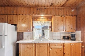 A kitchen with wooden cabinets, a white refrigerator, a sink, and a coffee maker. - Book multiple lakefront cottages at Sunnyside, from cozy studios to a 4BR home. (Greenbush)