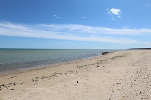 Ein weiter Sandstrand mit ruhigem Wasser, blauem Himmel und weiter Küste im Hintergrund.