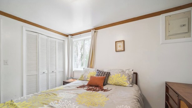 Un dormitorio con cama, mesita de noche, cómoda de madera, ventana con cortinas y un cuadro en la pared.