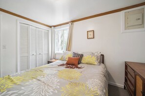 A bedroom with a bed, a nightstand, a wooden dresser, a window with curtains, and a picture on the wall.