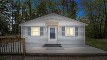 Une maison de plain-pied avec un porche à l’avant, une porte et deux fenêtres avec des volets.