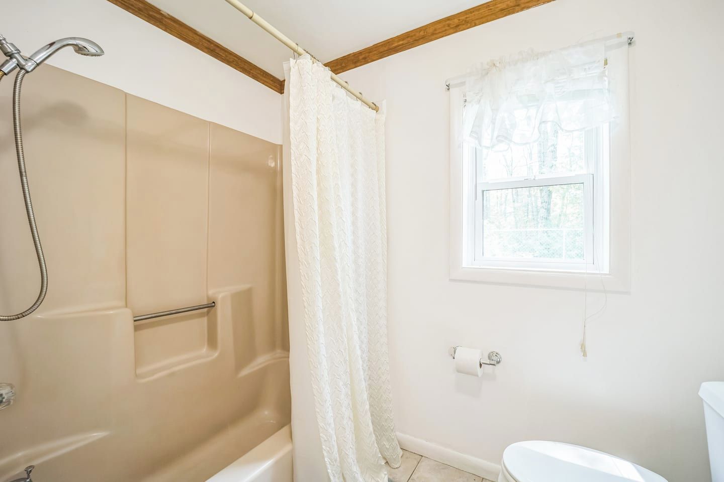 A bathroom with a shower, a toilet, and a window.