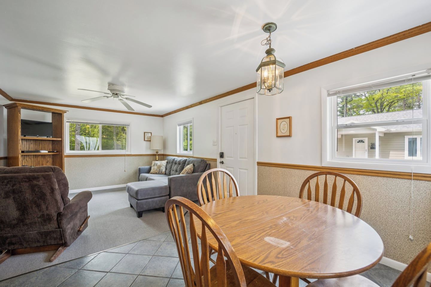 Un salon comprenant un canapé, un pouf et une table à manger avec des chaises. On y trouve également un ventilateur de plafond, une fenêtre avec vue et une lampe sur une table d’appoint.