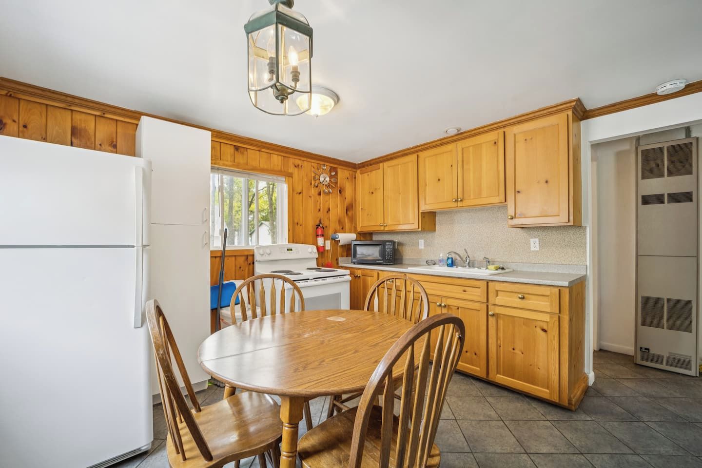 Une cuisine avec des meubles de rangement en bois, un réfrigérateur blanc, une cuisinière, un four à micro-ondes et une table à manger avec des chaises.