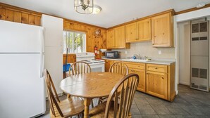 Una cocina con armarios de madera, un refrigerador blanco, una estufa, un microondas y una mesa de comedor con sillas.