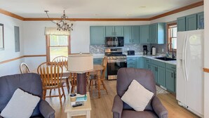 A modern kitchen with teal cabinets, a white refrigerator, and a dining area with wooden chairs and a table. - The biggest cottage at Sunnyside — newly remodeled, 4BR/3BA, sleeps up to 10. (Greenbush)