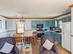 A modern kitchen with teal cabinets, a white refrigerator, and a dining area with wooden chairs and a table. - The biggest cottage at Sunnyside — newly remodeled, 4BR/3BA, sleeps up to 10. (Greenbush)