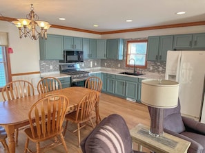A kitchen with teal cabinets, a dining table with chairs, a chandelier, and a refrigerator. - Cottage 6 - 4BR Lakefront Escape | Perfect for Groups! (Greenbush)