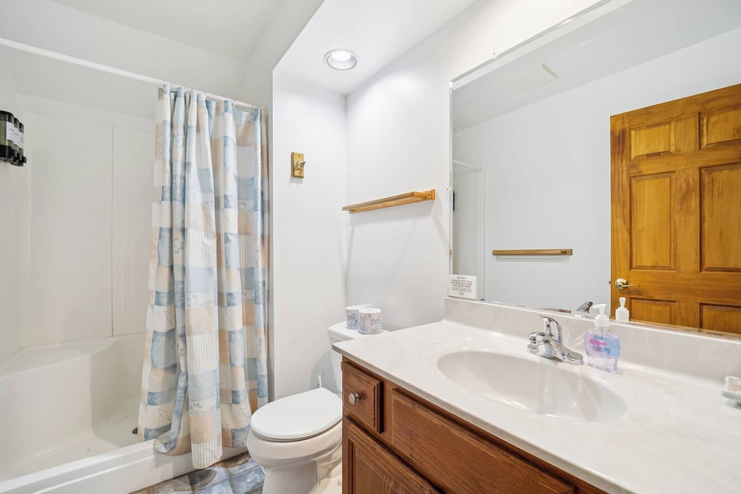 A bathroom with a shower, toilet, sink, and a wooden door.