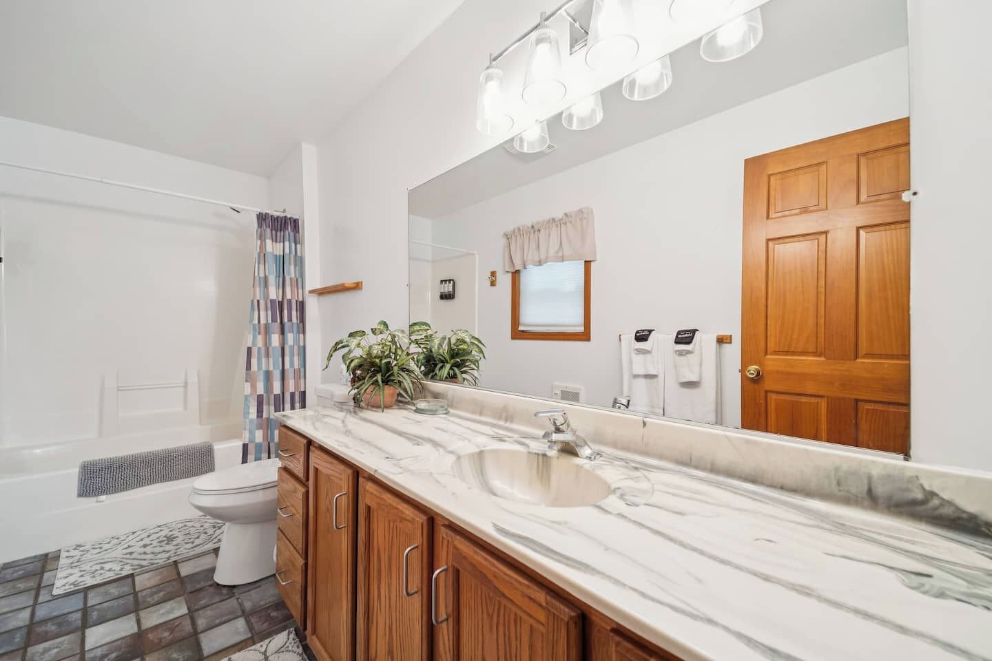 Une salle de bain avec un lavabo en marbre, des meubles en bois, un rideau de douche et un grand miroir.