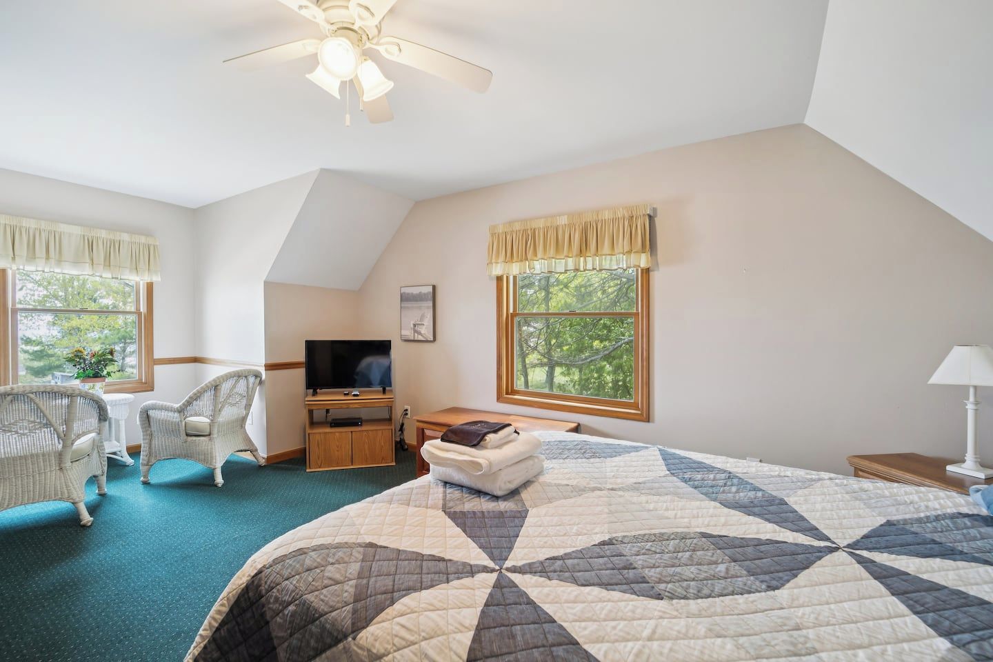 A hotel room with a bed, a desk, a television, two chairs, and a ceiling fan.