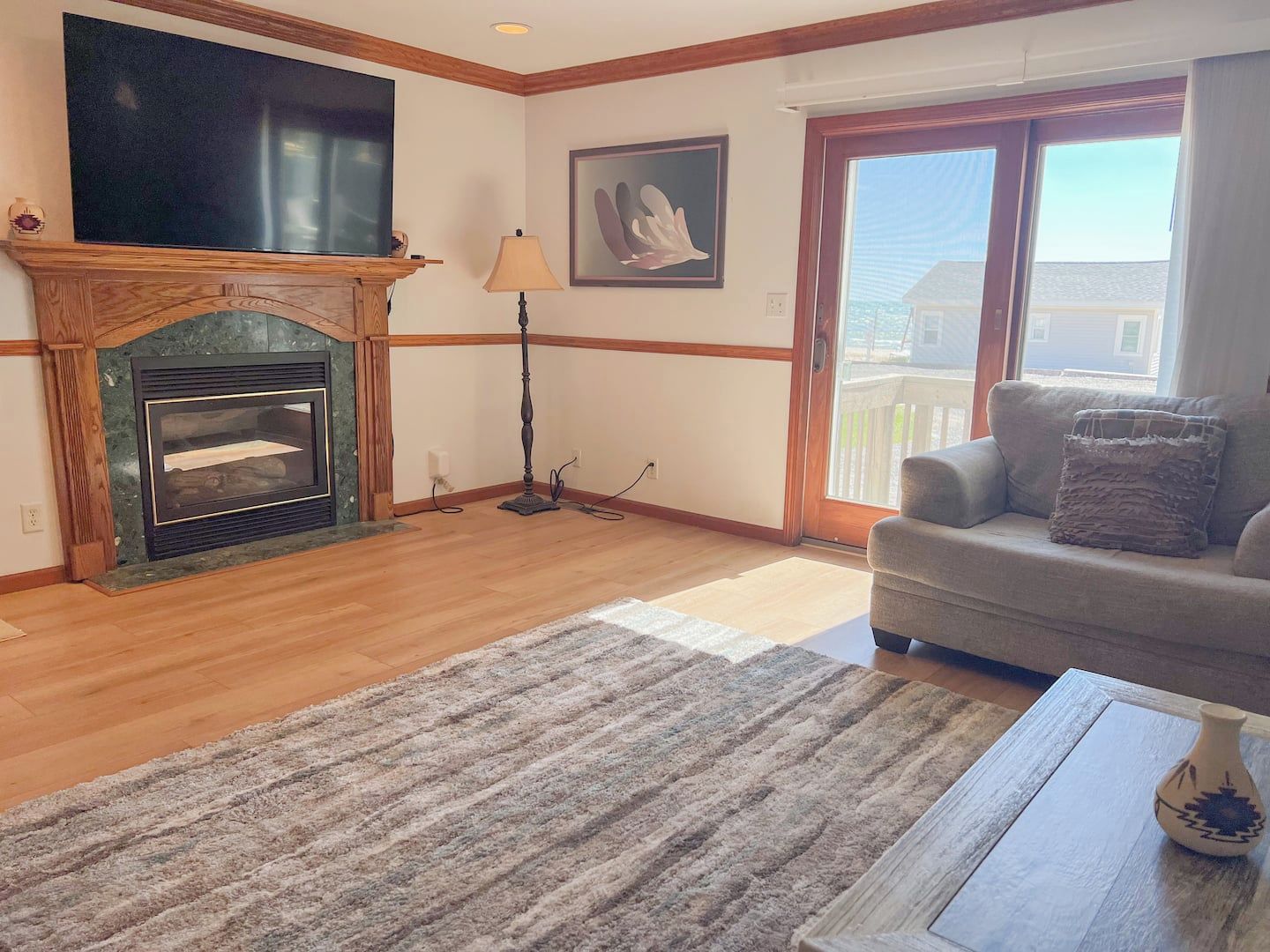 A living room with a fireplace, a television, a sofa, and a view through a glass door.
