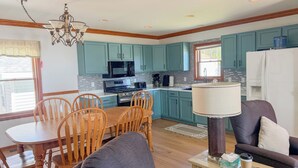 A modern kitchen with teal cabinets, a dining area with wooden chairs, and a living space with a sofa and coffee table. - The biggest cottage at Sunnyside — newly remodeled, 4BR/3BA, sleeps up to 10. (Greenbush)