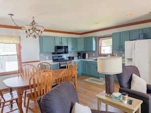A modern kitchen with teal cabinets, a dining area with wooden chairs, and a living space with a sofa and coffee table. - The biggest cottage at Sunnyside — newly remodeled, 4BR/3BA, sleeps up to 10. (Greenbush)