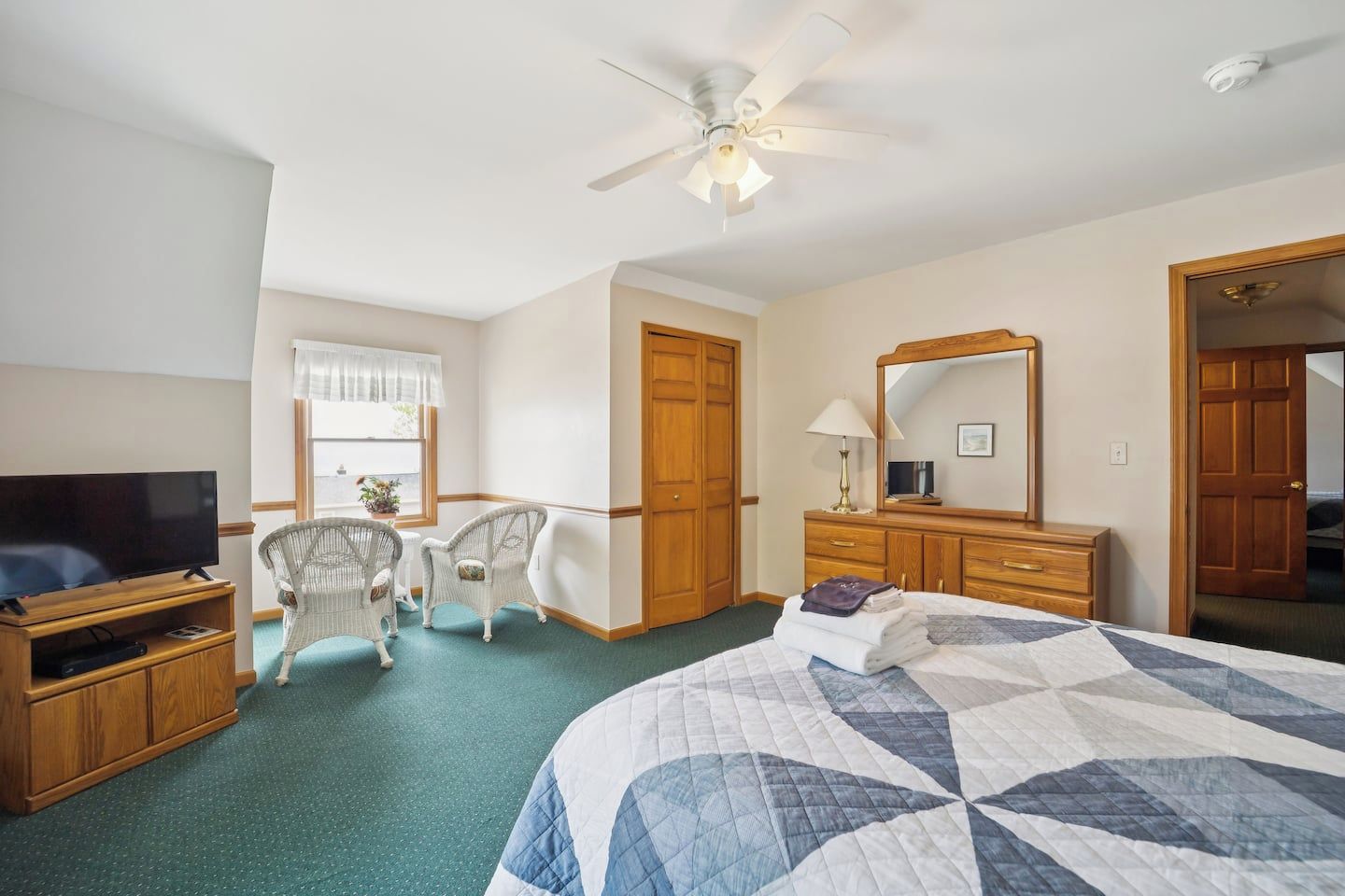 Une chambre d’hôtel équipée d’un lit, d’une télévision, d’un bureau, d’une chaise, d’une armoire et d’un ventilateur de plafond.