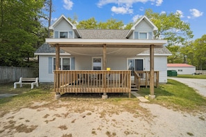 A two-story house with a covered porch and a front door. - The biggest cottage at Sunnyside — newly remodeled, 4BR/3BA, sleeps up to 10. (Greenbush)