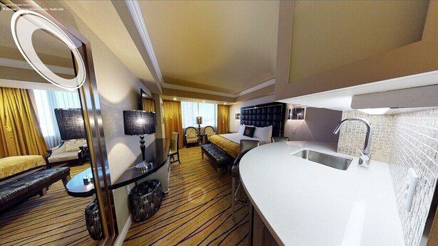 A hotel room with a bed, a sofa, a small table, a mirror, a TV, and a bathroom with a sink and shower.