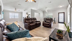 A spacious living room with leather sofas, a coffee table, and a ceiling fan.