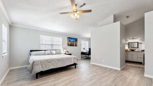 A spacious bedroom with a large bed, a desk, and a view of a kitchen area.