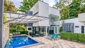 Ein modernes Haus mit Pool, Sitzgelegenheiten im Freien und einer überdachten Terrasse.